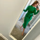 A woman takes a mirror selfie wearing a bright green long-sleeve midi dress with a tie-waist detail, standing in a home hallway.